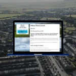 Millom Town Council website showing meeting minutes page with sidebar navigation and document viewer on blue laptop against aerial view of Millom